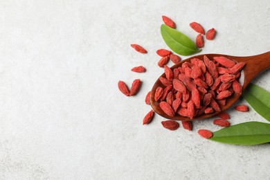 Photo of Dried goji berries, leaves and spoon on light textured table, flat lay. Space for text