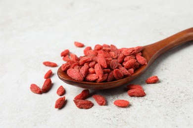 Photo of Dried goji berries and spoon on light textured table, closeup