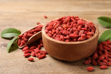 Photo of Dried goji berries, leaves, bowl and scoop on wooden table, closeup