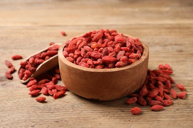 Photo of Dried goji berries, bowl and scoop on wooden table, closeup