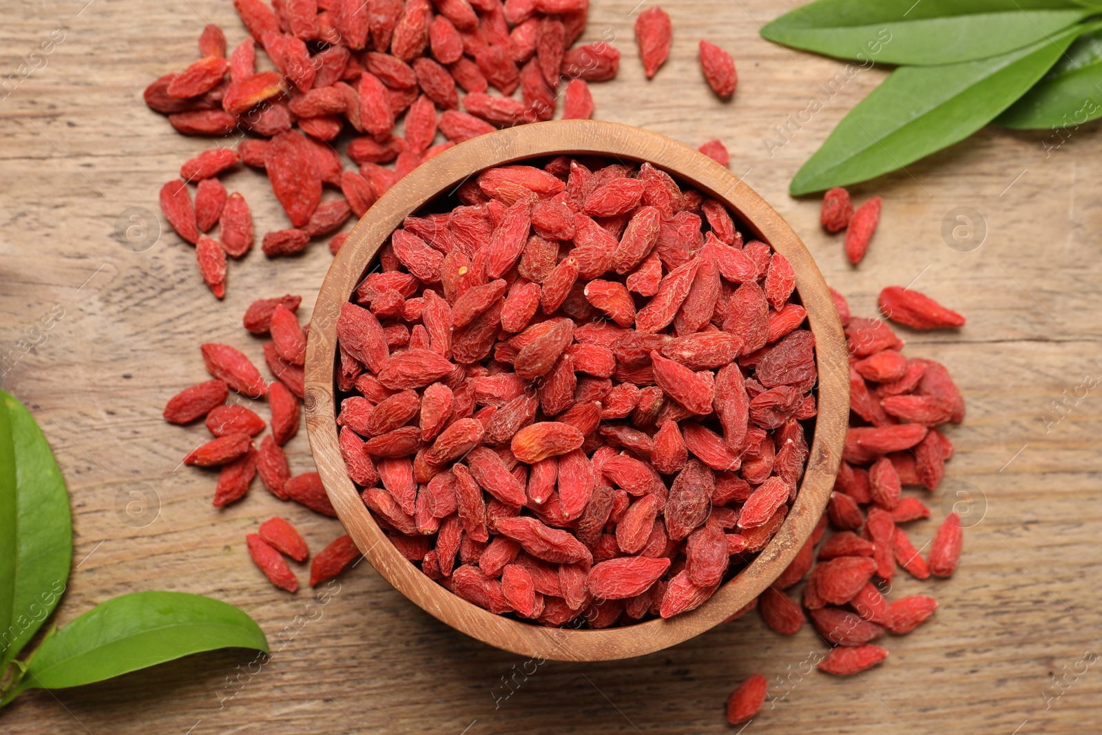 Photo of Dried goji berries, leaves and bowl on wooden table, flat lay