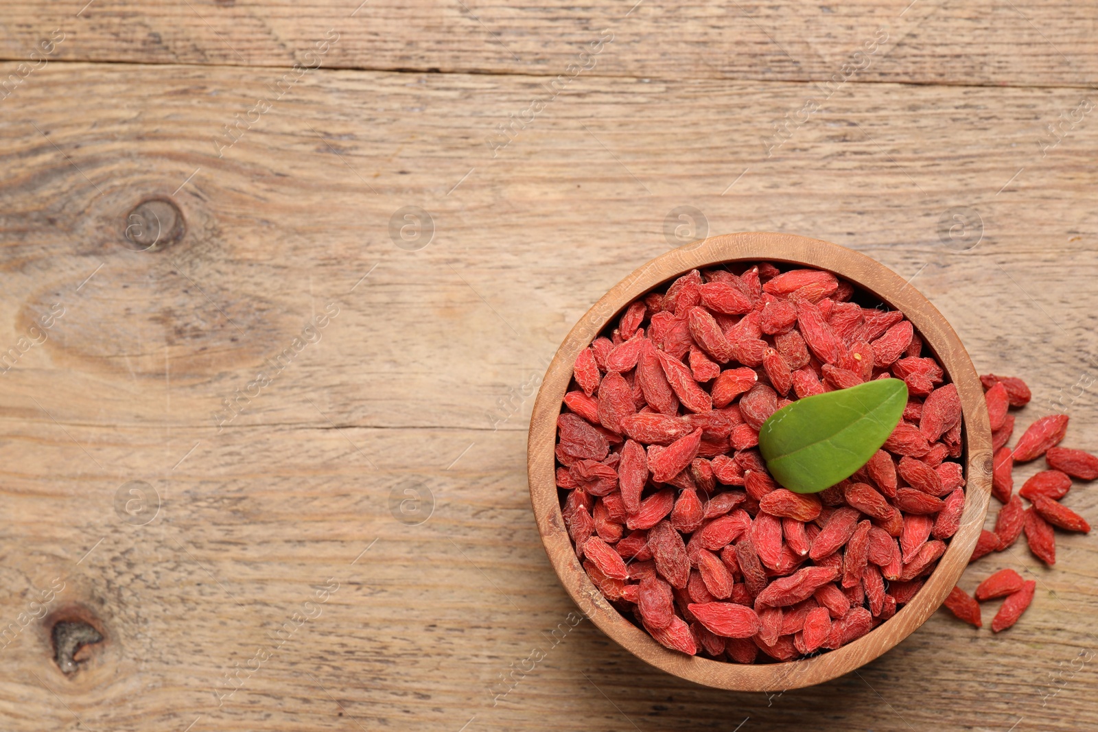 Photo of Dried goji berries in bowl on wooden table, top view. Space for text