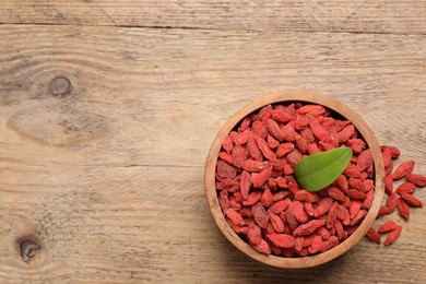 Photo of Dried goji berries in bowl on wooden table, top view. Space for text