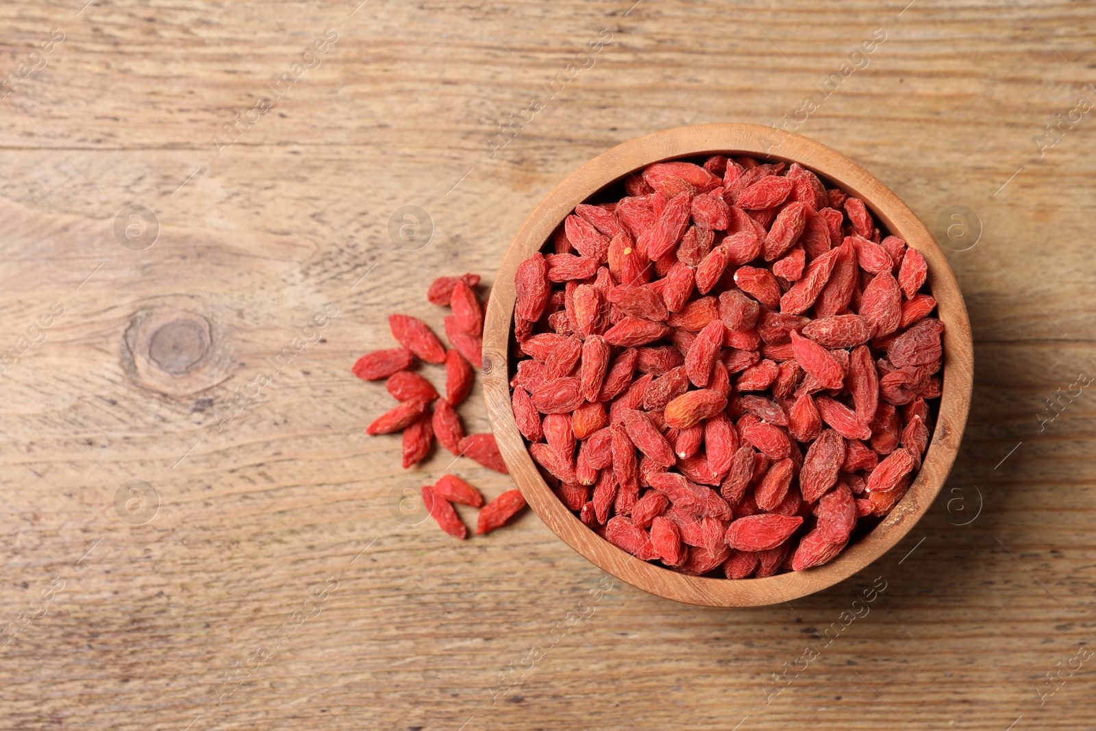 Photo of Dried goji berries in bowl on wooden table, top view. Space for text