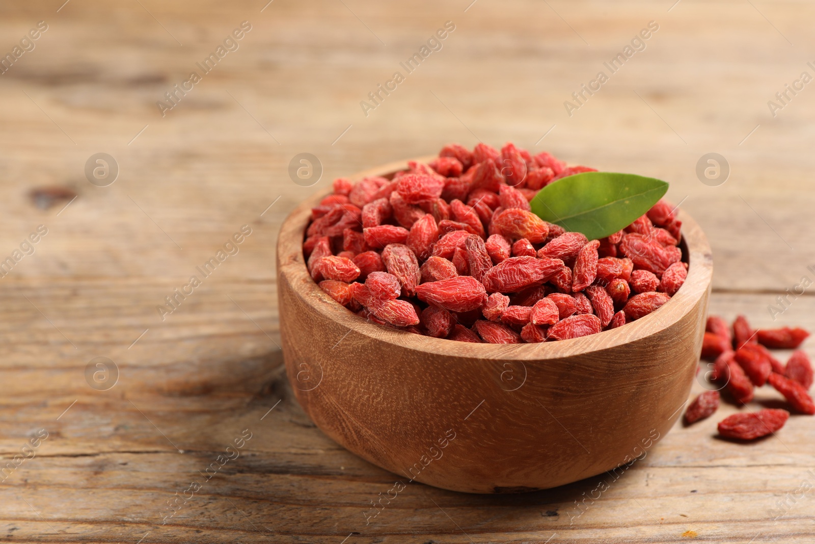 Photo of Dried goji berries and leaf in bowl on wooden table, closeup. Space for text