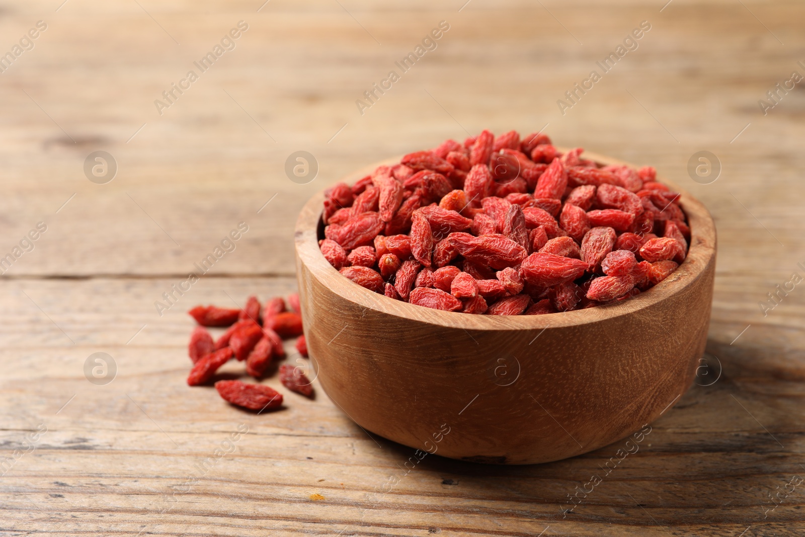 Photo of Dried goji berries in bowl on wooden table, closeup. Space for text