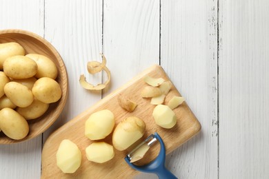 Photo of Fresh raw potatoes, peels and peeler on white wooden table, top view