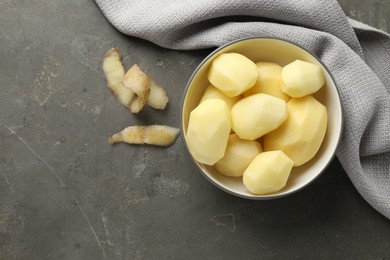 Photo of Fresh raw potatoes in bowl and peels on grey table, top view. Space for text