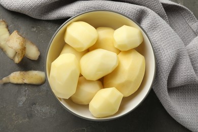 Fresh raw potatoes in bowl and peels on grey table, top view