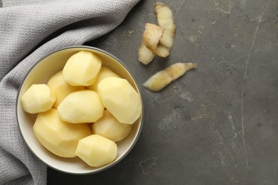 Fresh raw potatoes in bowl and peels on grey table, top view. Space for text