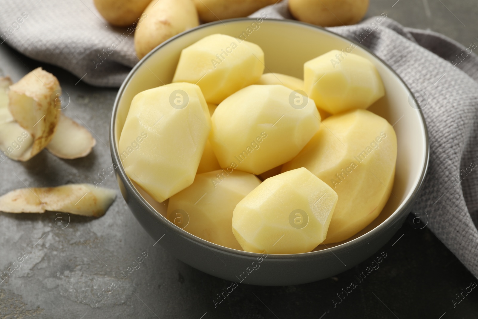 Photo of Fresh raw potatoes and peels on grey table