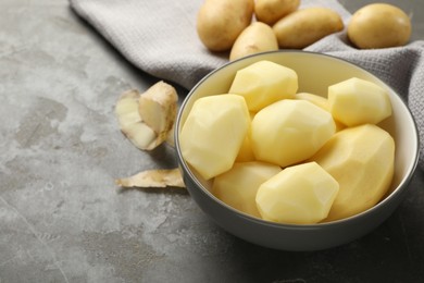 Photo of Fresh raw potatoes and peels on grey table, space for text