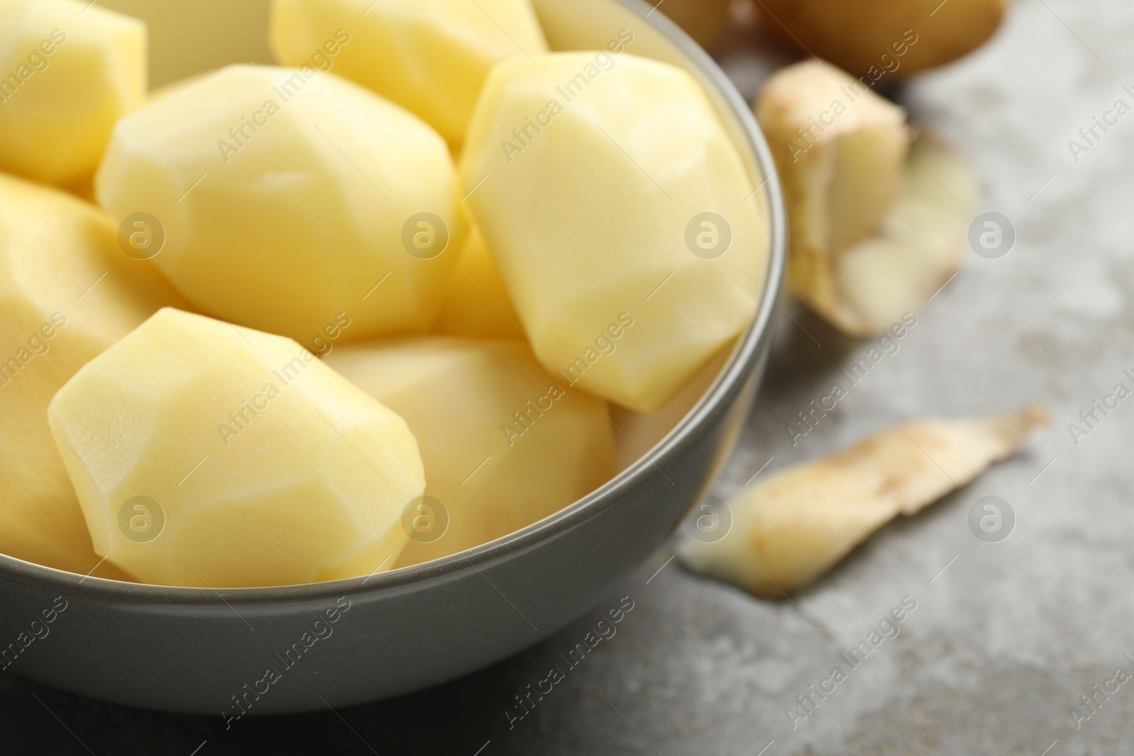 Photo of Fresh raw potatoes in bowl on grey table, closeup