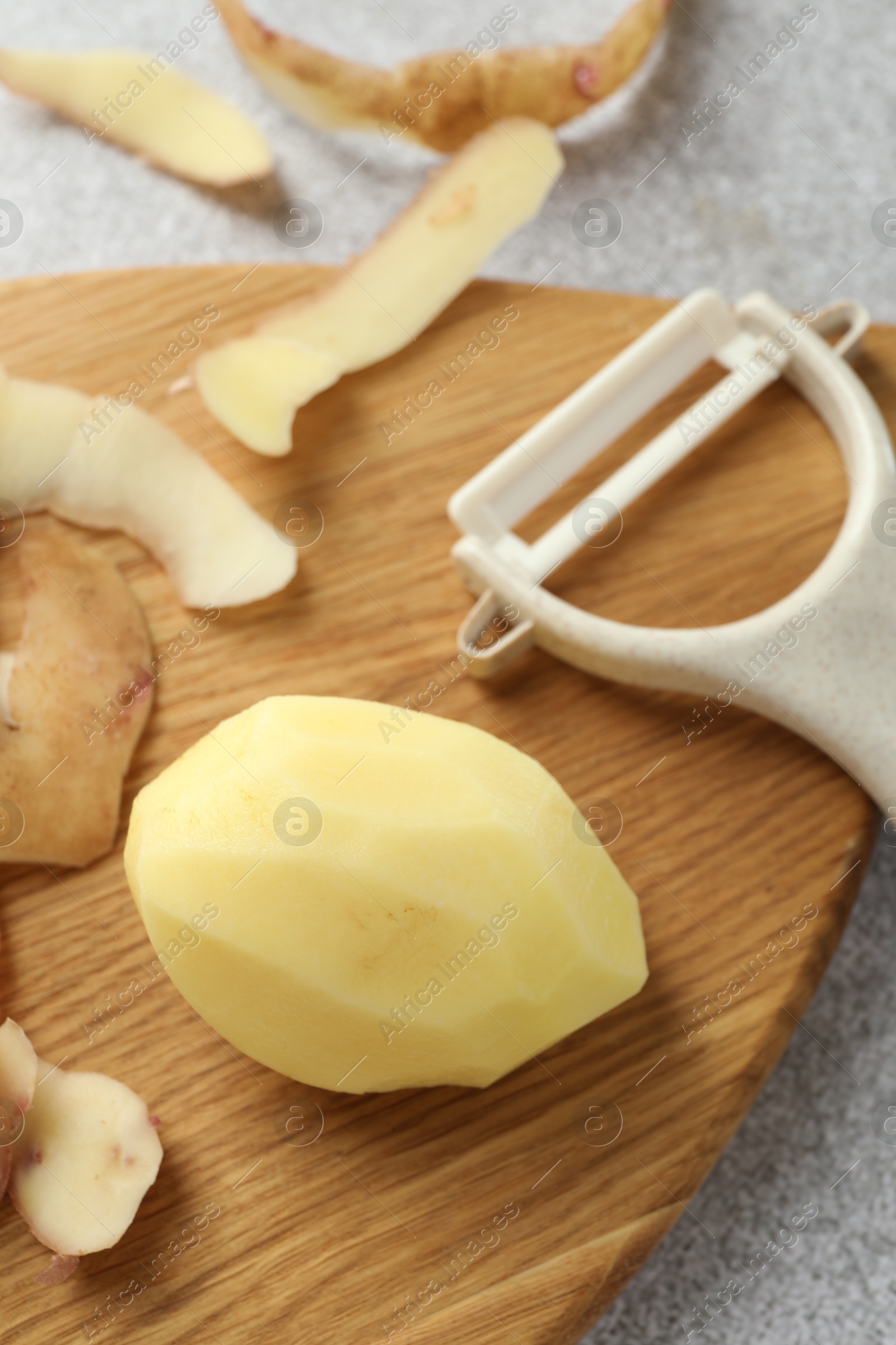 Photo of Fresh raw potato, peels and peeler on light grey table