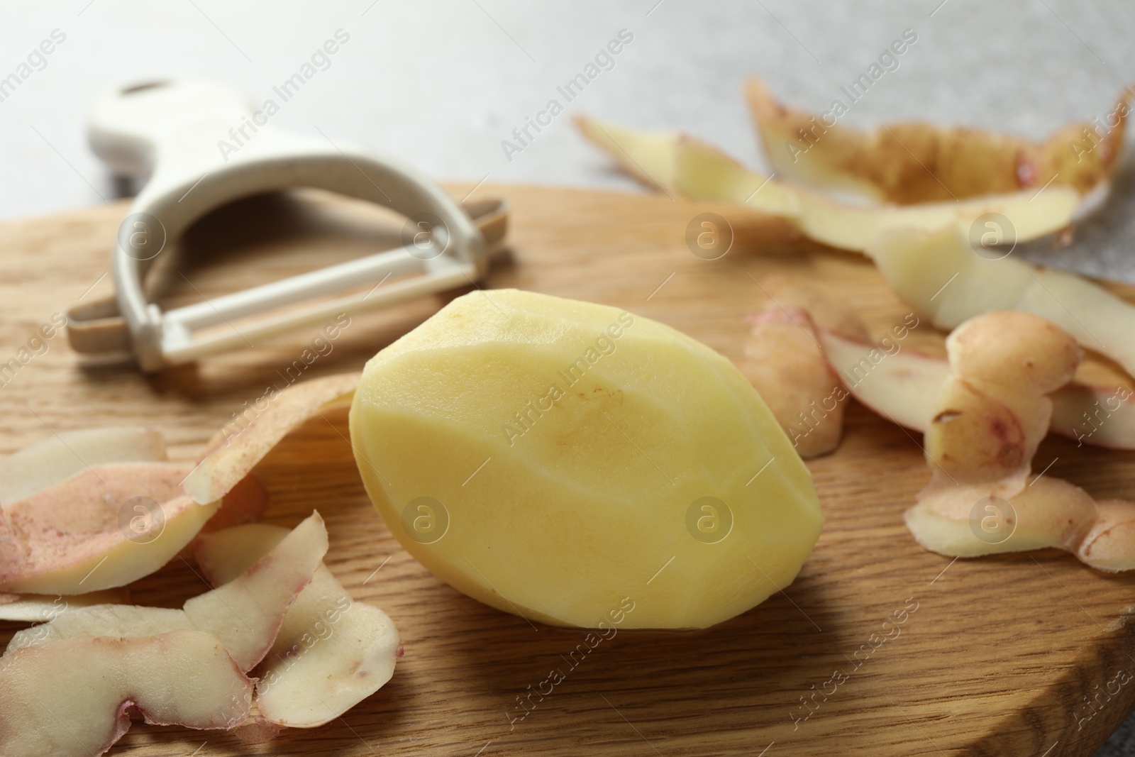 Photo of Fresh raw potato, peels and peeler on table, closeup