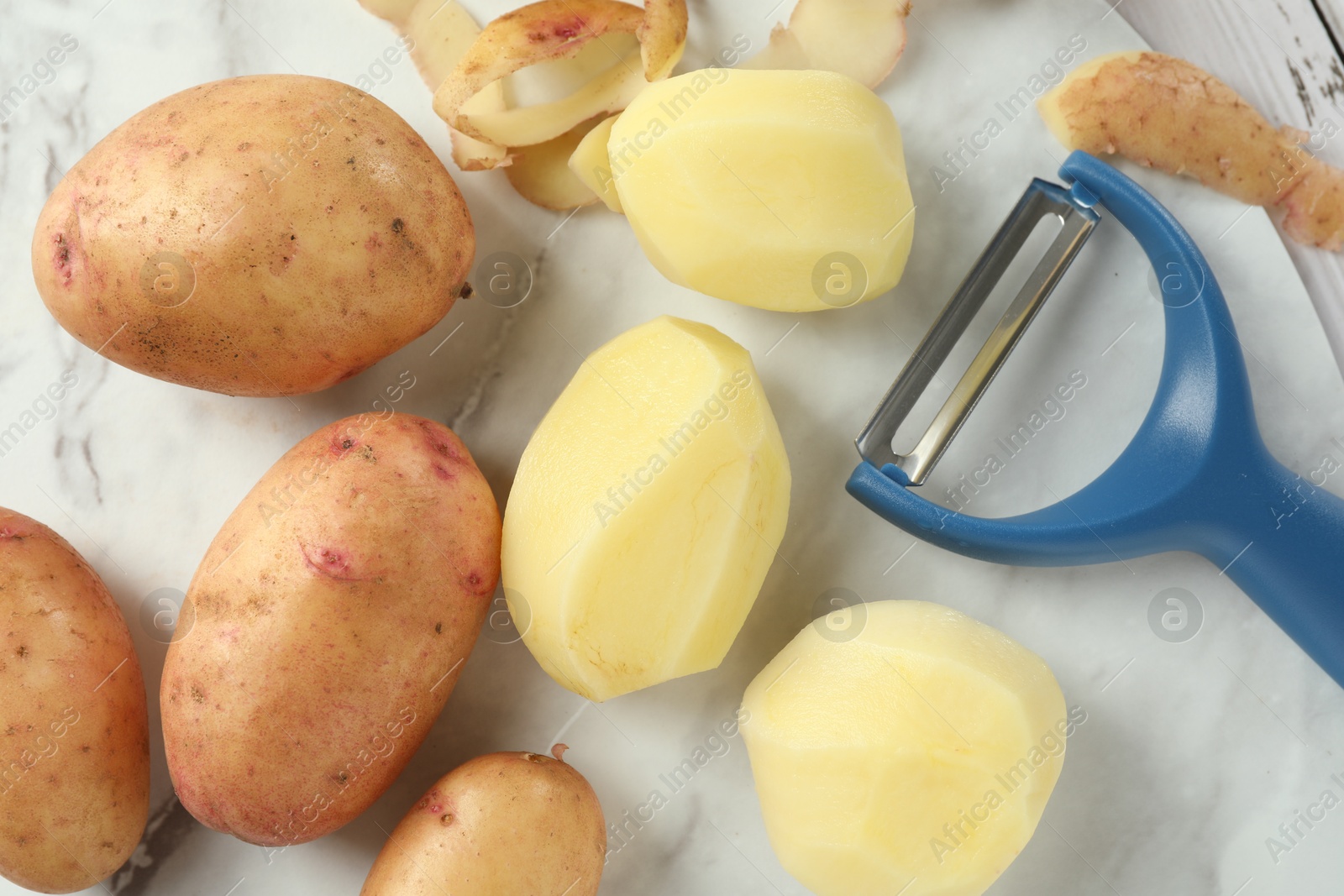 Photo of Fresh raw potatoes, peels and peeler on table, top view