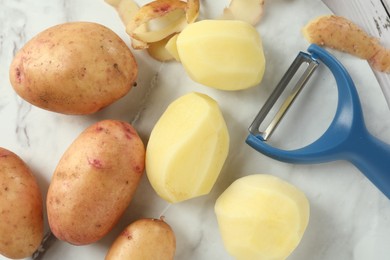 Photo of Fresh raw potatoes, peels and peeler on table, top view