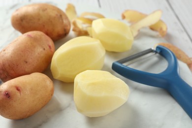 Fresh raw potatoes, peels and peeler on table