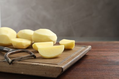 Photo of Fresh raw potatoes and peeler on wooden table. Space for text