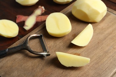 Fresh raw potatoes, peels and peeler on table