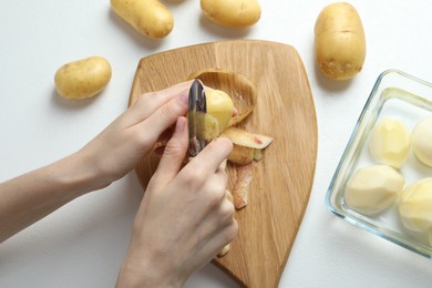 Photo of Woman peeling fresh potato with peeler at white table, top view