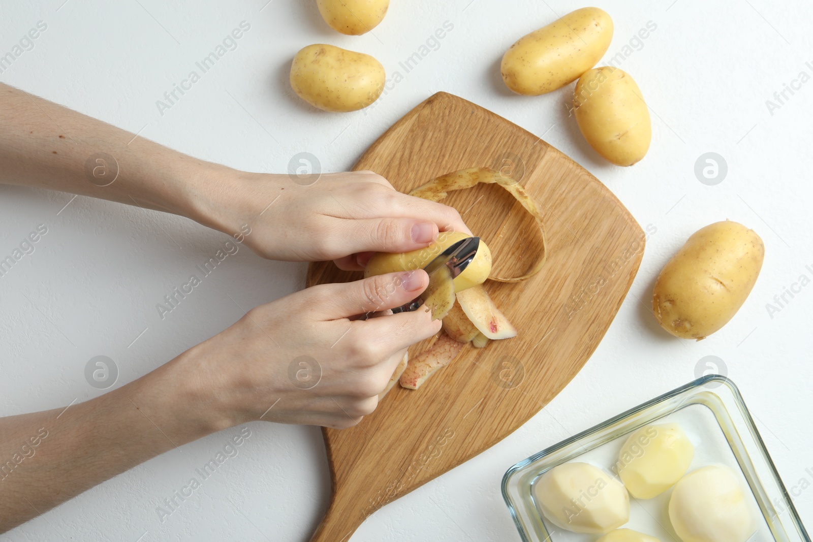 Photo of Woman peeling fresh potato with peeler at white table, top view