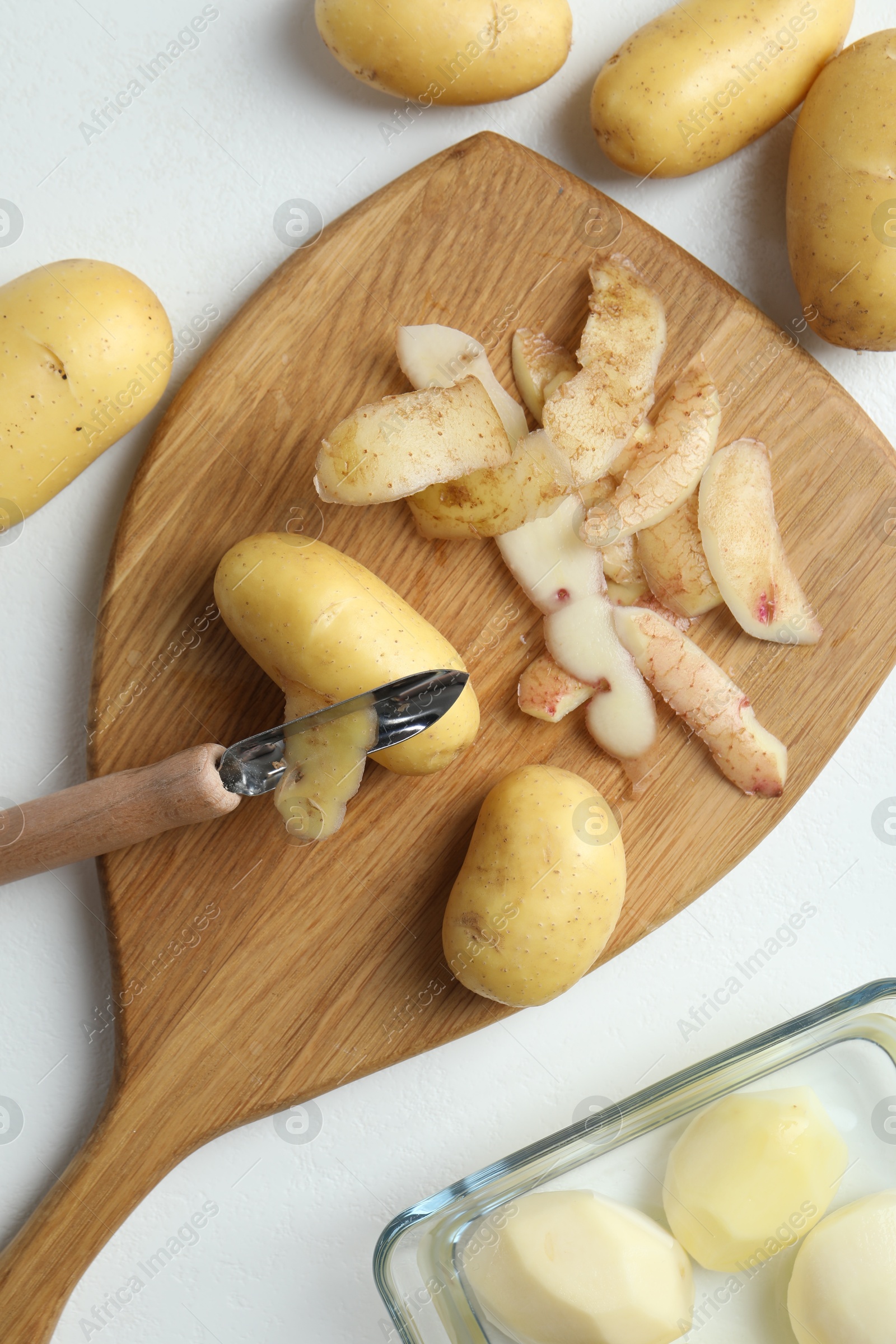 Photo of Fresh raw potatoes, peels and peeler on white table, top view