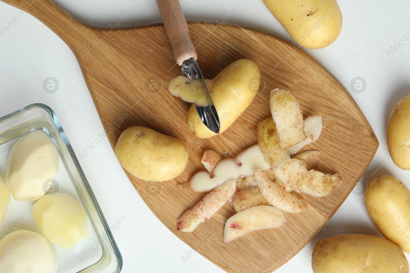 Photo of Fresh raw potatoes, peels and peeler on white table, top view