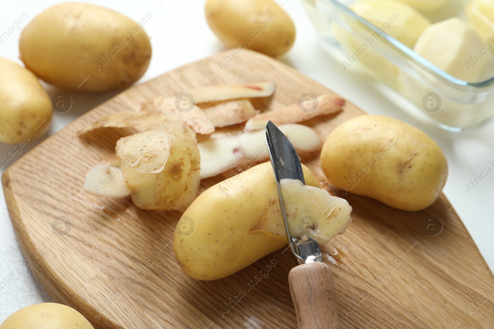 Photo of Fresh raw potatoes, peels and peeler on table