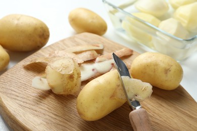 Fresh raw potatoes, peels and peeler on white table