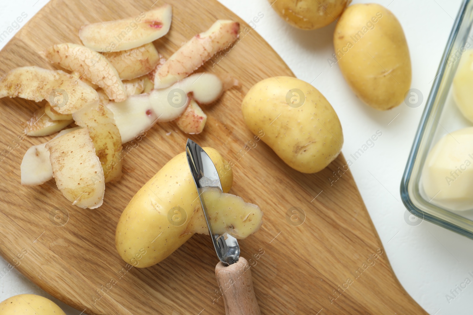 Photo of Fresh raw potatoes, peels and peeler on white table, top view