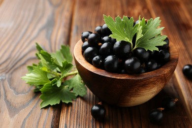 Ripe black currants and leaves in bowl on wooden table, closeup. Space for text