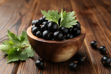 Ripe black currants and leaves in bowl on wooden table