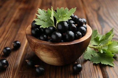 Ripe black currants and leaves in bowl on wooden table