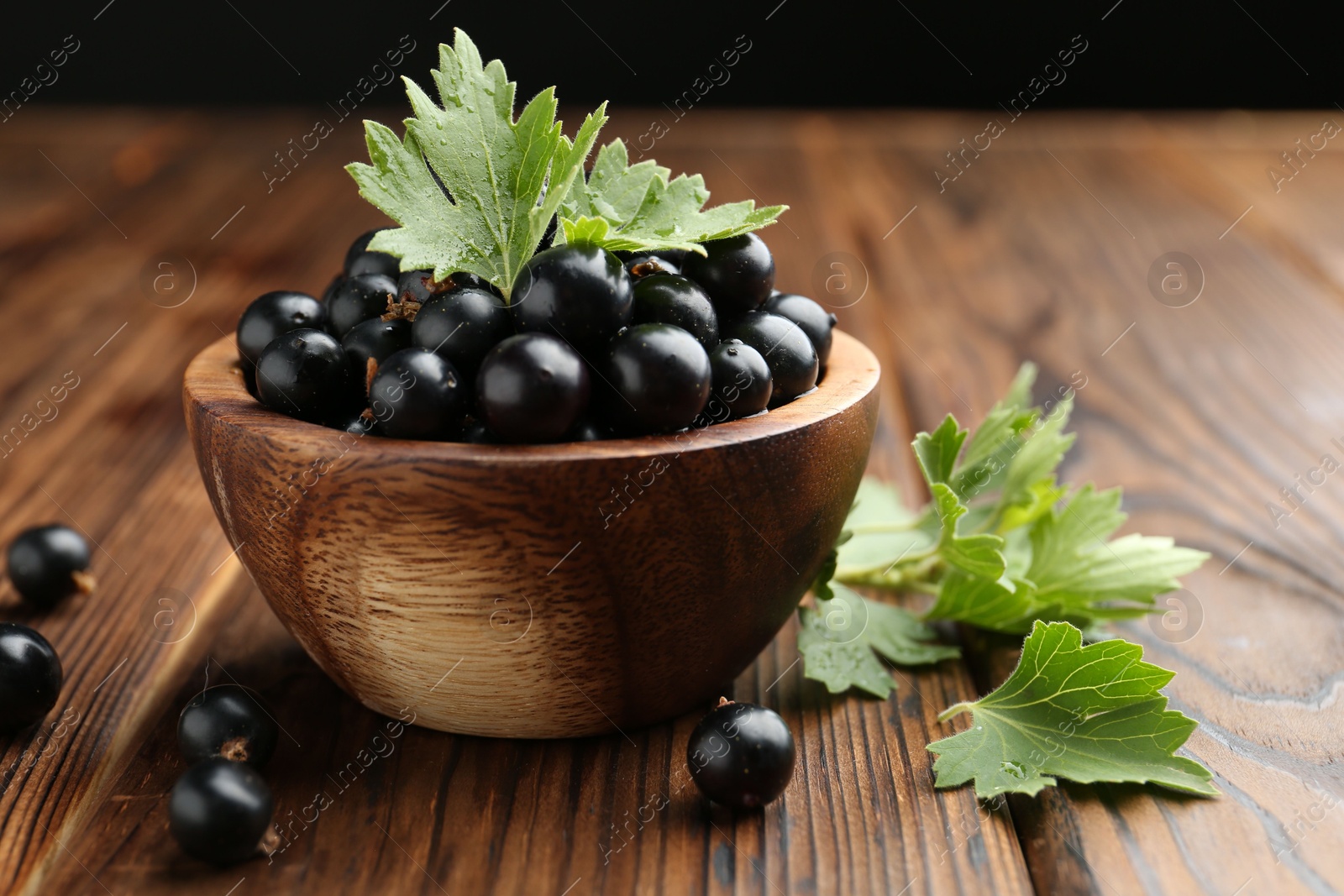 Photo of Ripe black currants and leaves in bowl on wooden table