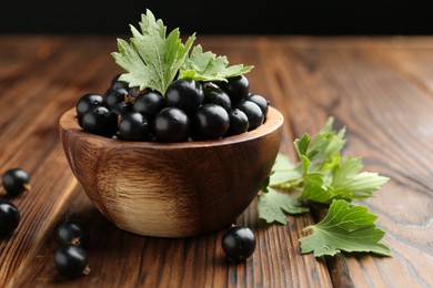 Ripe black currants and leaves in bowl on wooden table