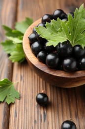 Ripe black currants and leaves in bowl on wooden table, closeup