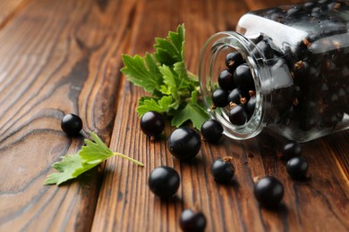 Ripe black currants and leaves in jar on wooden table, closeup. Space for text