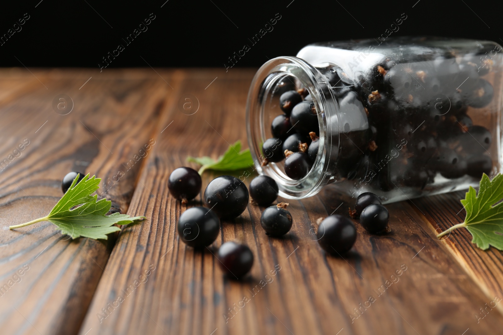 Photo of Ripe black currants and leaves in jar on wooden table, closeup. Space for text