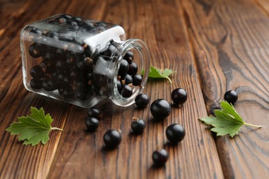 Ripe black currants and leaves in jar on wooden table, space for text