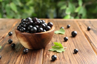 Ripe black currants and leaves in bowl on wooden table, space for text