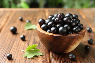 Photo of Ripe black currants and leaves in bowl on wooden table, closeup. Space for text