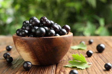 Ripe black currants and leaves in bowl on wooden table, closeup. Space for text