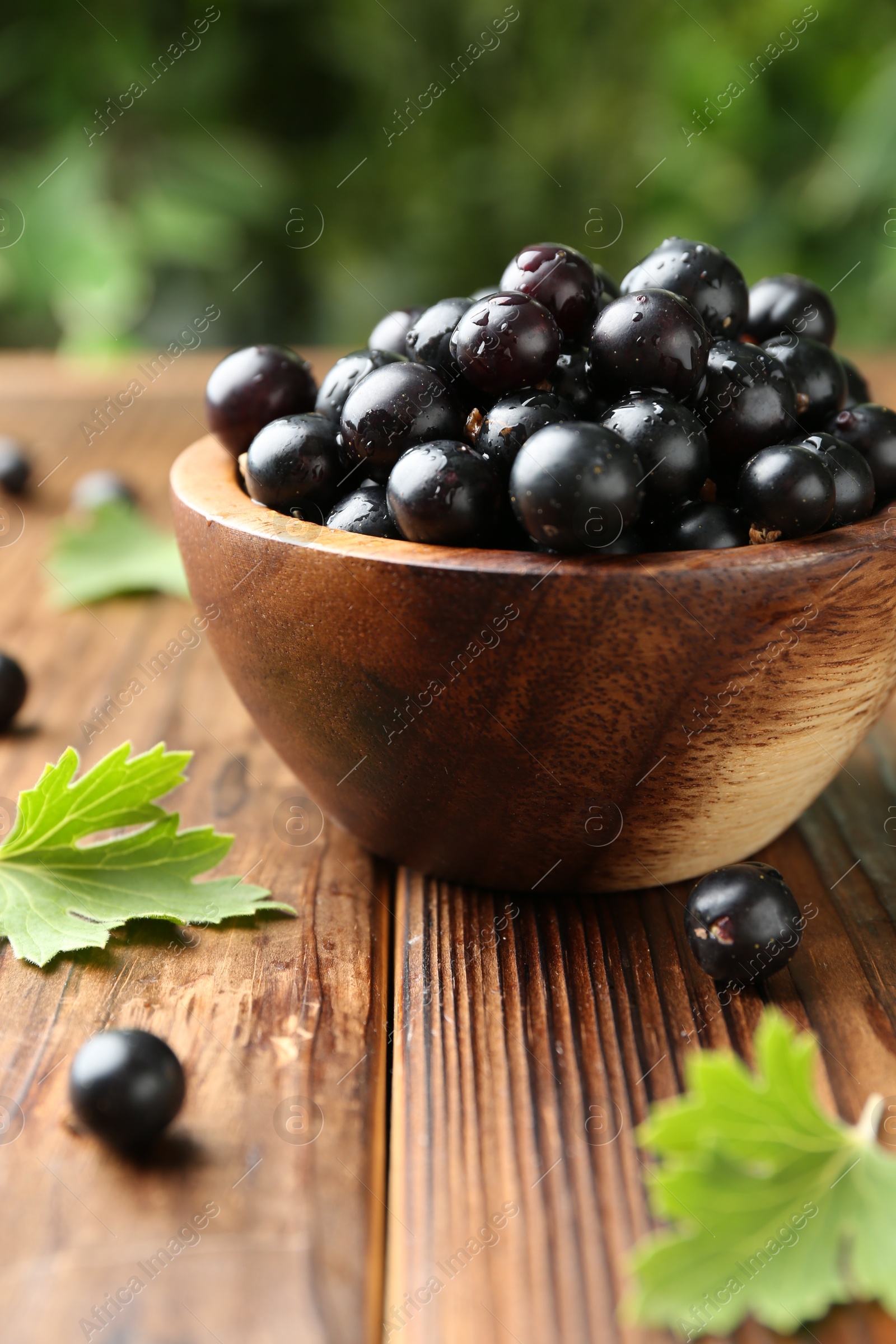 Photo of Ripe black currants and leaves in bowl on wooden table