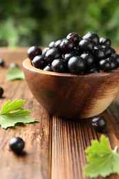 Ripe black currants and leaves in bowl on wooden table