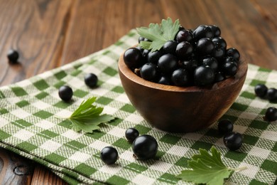 Photo of Ripe black currants and leaves in bowl on wooden table, space for text