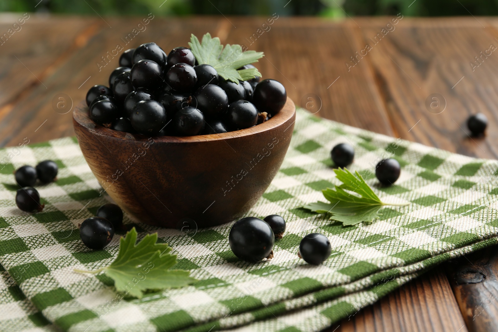 Photo of Ripe black currants and leaves in bowl on wooden table, space for text