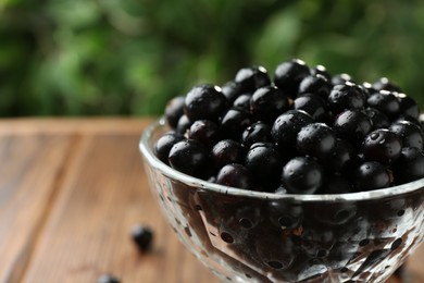 Photo of Ripe black currants in glass on wooden table, closeup. Space for text