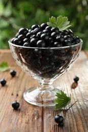 Ripe black currants and leaves in glass on wooden table