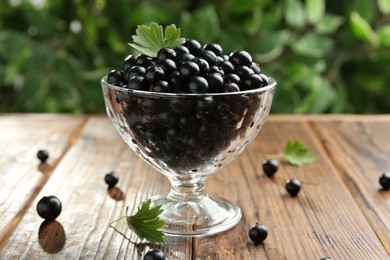 Photo of Ripe black currants and leaves in glass on wooden table